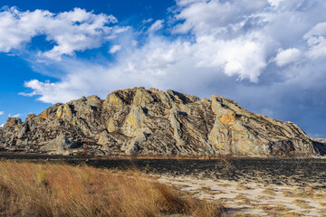 Dramatic layered sandstone cliffs rise above dry savanna grassland under bright blue sky with scattered white clouds. Jurassic geological formations at Isalo National Park, Madagascar.