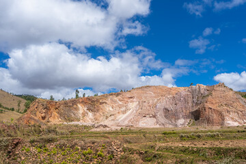 Dramatic rocky cliff face showing colorful sedimentary layers of pink, brown and white stone. Natural geological formations with sparse vegetation, near Isalo National Park, Madagascar.