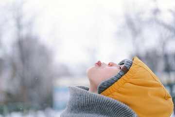 A joyful child enjoys the winter weather, bundled in warm clothing including a bright yellow jacket...