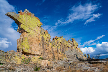 Weathered sandstone cliff with monster-like silhouette, covered in yellow-green lichen against vivid blue sky. Popular 