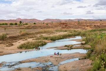 Local women washing clothes by the river with scenic rocky formations in the background. The landscape showcases the daily life of the local community. Isalo National Park, Madagascar.