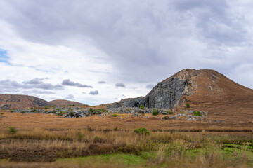 A rugged hill with rocky outcrops under a cloudy sky. Dry grassland surrounds the hill. Isalo National Park, Madagascar.