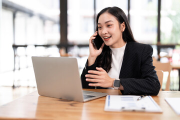 Happy businesswoman talking on mobile phone while using laptop at office.