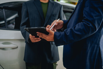 Asian clients engage with a car insurance agent beside a wrecked vehicle. They examine the policy details, assess the damage, and finalize paperwork related to the insurance claim and repairs.