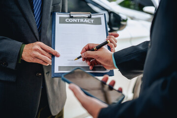 An Asian businessman buys a car, signs a contract with the salesman, and receives the keys. They discuss essential terms, covering car leasing, finance, and loan laws to finalize the purchase