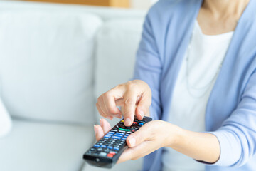 リビングでテレビリモコンを操作するシニア女性