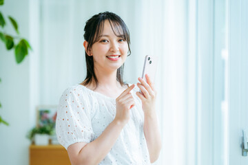 部屋でスマホを操作する若い女性