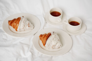 croissants on plates, cups of coffee on the white bed sheet.