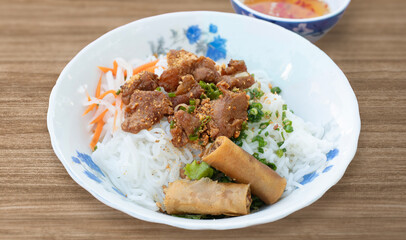 A bowl of Vermicelli Noodles with Grilled Pork and Egg Rolls, Vietnamese grilled pork and rice noodles. Bun thit nuong. Fried Spring Rolls Cold Rice Vermicelli with sauce served in bowl isolated. 