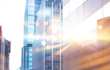 A city skyline with tall buildings and bright sunlight shining through the glass.