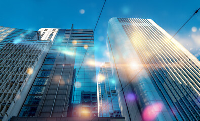 A low angle view of tall buildings against a bright blue sky with a lens flare effect.