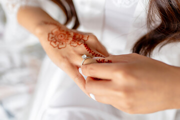 Hands of bride with henna tattoo and wedding ring on finger close-up. The bride takes off or puts on a wedding ring on her finger. Hands of the bride with a gold engagement ring with a diamond