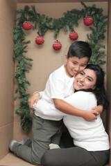 Latino mom and son inside a cardboard gift box show their love to celebrate Christmas and New Year