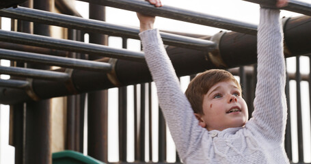 Obraz premium Boy, child and monkey bars at playground, outdoor and adventure with smile, learning and balance. Kid, happy and exercise with swing on jungle gym at park for challenge, climbing or sunshine in Spain