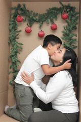 Latino mom and son inside a cardboard gift box show their love to celebrate Christmas and New Year