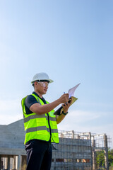 Portrait of a construction engineer standing in front of a building under construction while reviewing the building construction plans.