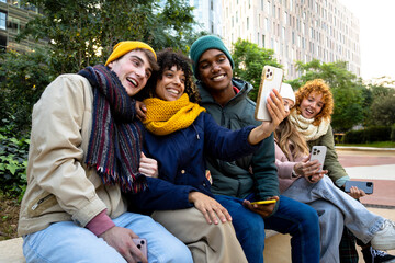 Happy multiracial smiling and cheerful college student friends taking selfie together in a winter day using mobile phone