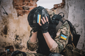 A soldier in uniform with a machine gun sits on the ruins of a destroyed building and covers his face with his hand. Post-traumatic stress disorder concept