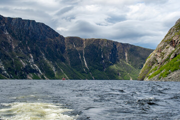 A tiny ship navigates the waters beneath the towering cliffs of Western Brook Pond, emphasizing the immense scale and breathtaking majesty of Gros Morne National Park's stunning landscape.