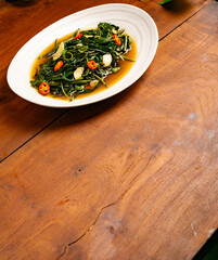 Stir fried water spinach with chili garnish on a wooden table. "Sayur Kangkung" vegetable from Indonesia.
