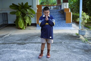 A smiling boy raises his hand to say hello in Thai style.