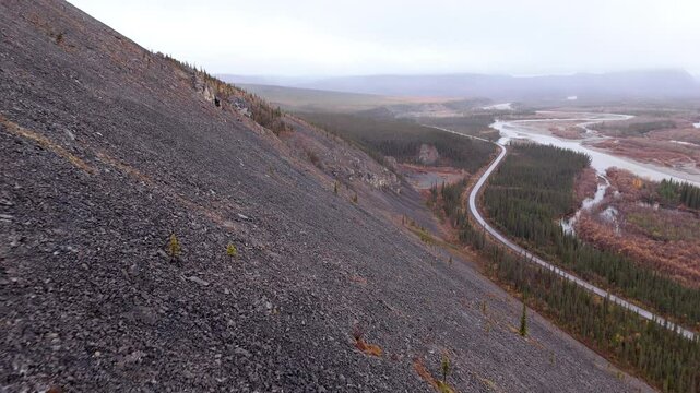 Rocky And Treeless Mountain Slope With Dempster Highway And River In Yukon, Canada. - aerial shot