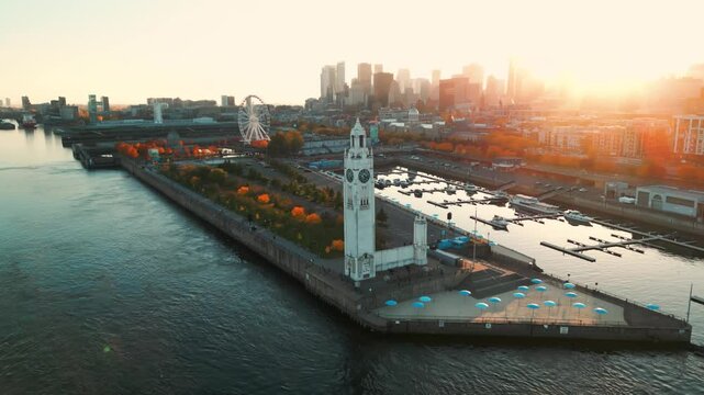 orbital aerial shot around the clock tower in the ol port in Montreal city with ferris wheel and the skyline in the background at sunset during fall season, quebec province, canada