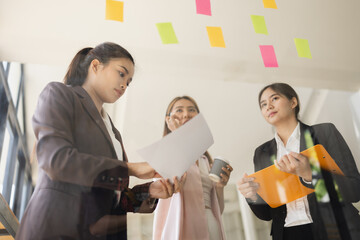 Asian businesswoman teamwork planning with sticky notes and new ideas on a glass wall, Business people brainstorming strategy and new ideas concept, startup worker meeting,