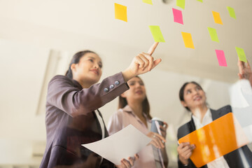 Asian businesswoman teamwork planning with sticky notes and new ideas on a glass wall, Business people brainstorming strategy and new ideas concept, startup worker meeting,