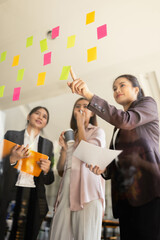 Asian businesswoman teamwork planning with sticky notes and new ideas on a glass wall, Business...