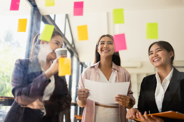 Asian businesswoman teamwork planning with sticky notes and new ideas on a glass wall, Business people brainstorming strategy and new ideas concept, startup worker meeting,