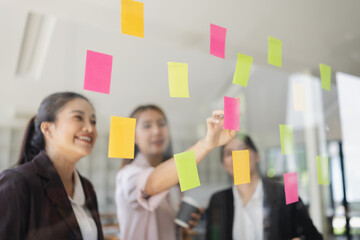Asian businesswoman teamwork planning with sticky notes and new ideas on a glass wall, Business...