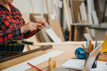 Woman in a red plaid shirt sharpening a pencil with a utility knife in a woodworking workshop. Ideal for carpentry, DIY projects, and banner displays with a focus on craftsmanship, Carpenter