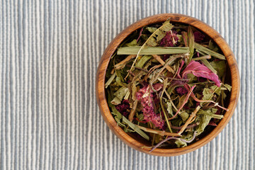 Wooden bowl filled with dried herbs for Ecuadorian horchata tea, placed on a striped blue and white fabric. Ideal for promoting natural remedies, herbal teas, and wellness products.