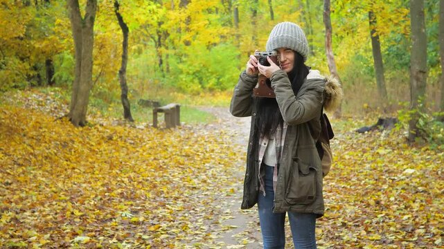 Traveling in nature. A young beautiful girl, in an autumn forest, enjoys the beauty of autumn nature, photographs objects she likes, smiles. Slow motion.
