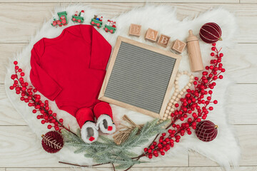A cozy holiday-themed pregnancy announcement setup with a baby onesie, doll, and festive...