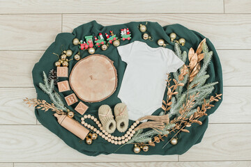 Festive baby announcement setup featuring a baby onesie, a letterboard, and seasonal holiday decorations on a soft background. Ideal for Christmas-themed baby reveal or holiday family announcement.