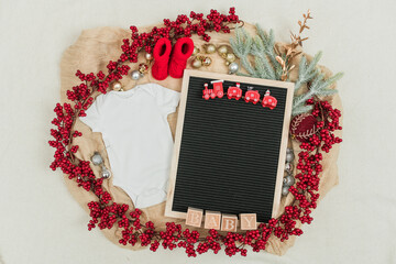 Festive baby announcement setup featuring a baby onesie, a letterboard, and seasonal holiday...