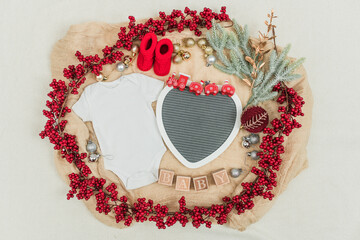 Festive baby announcement setup featuring a baby onesie, a letterboard, and seasonal holiday...