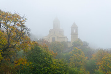 Naklejka premium Church of St. Ekvtime in Kiketi village on a foggy morning. Trees with autumn leaves, bushes in the foreground