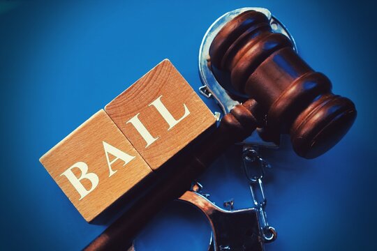 Word BAIL composed of wooden dices. Wooden gavel and statue of Themis in the background.