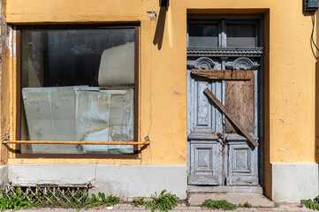 Weathered wooden door and boarded window of an abandoned building in a yellow-walled street