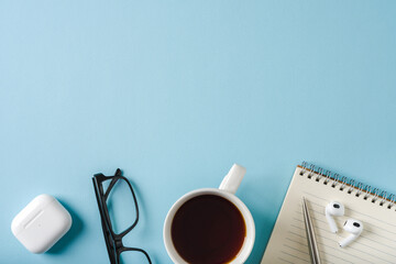 Top view of notebook, glasses, coffee, earphones and ballpoint pen on blue background