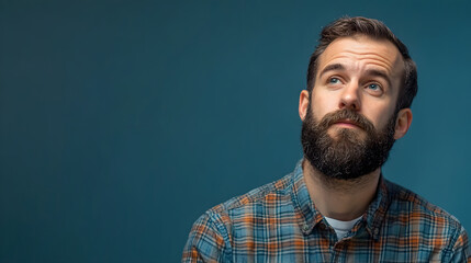 Obraz premium Man with beard in plaid shirt looking thoughtfully upwards