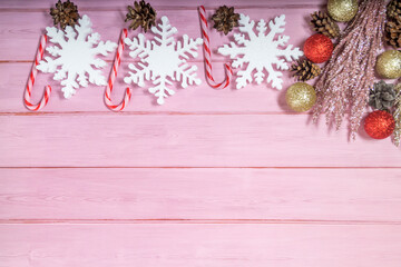 Christmas decorations on a pink wooden background: balls, branches, snowflakes and candy canes, top view, copyspace