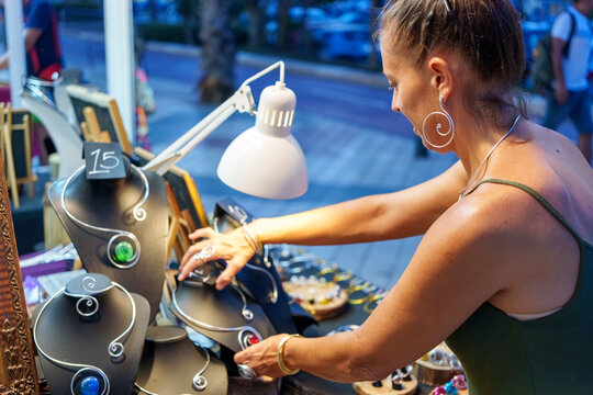 Mature Woman Organizing Display of Handmade Aluminum Wire Jewelry at Outdoor Market Stall