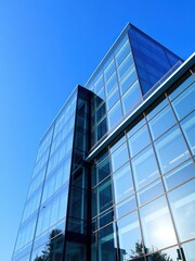 Modern office building with sleek glass exterior, set against a vibrant blue sky, business, reflection, modern