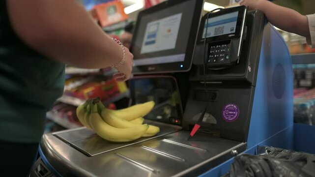 person scans bananas at self-checkout station in grocery store, with screen and payment terminal in view, reflecting modern shopping experience. scans bananas at self-checkout station, grocery store