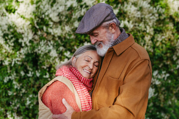 Fototapeta premium Portrait of beautiful senior couple outdoors in an autumn garden. Elderly husband and wife are embracing each other.