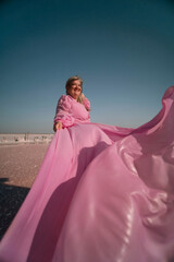 Fototapeta premium Woman Pink Dress Salt Flats - A woman in a pink dress poses on a salt flat with a bright blue sky in the background.